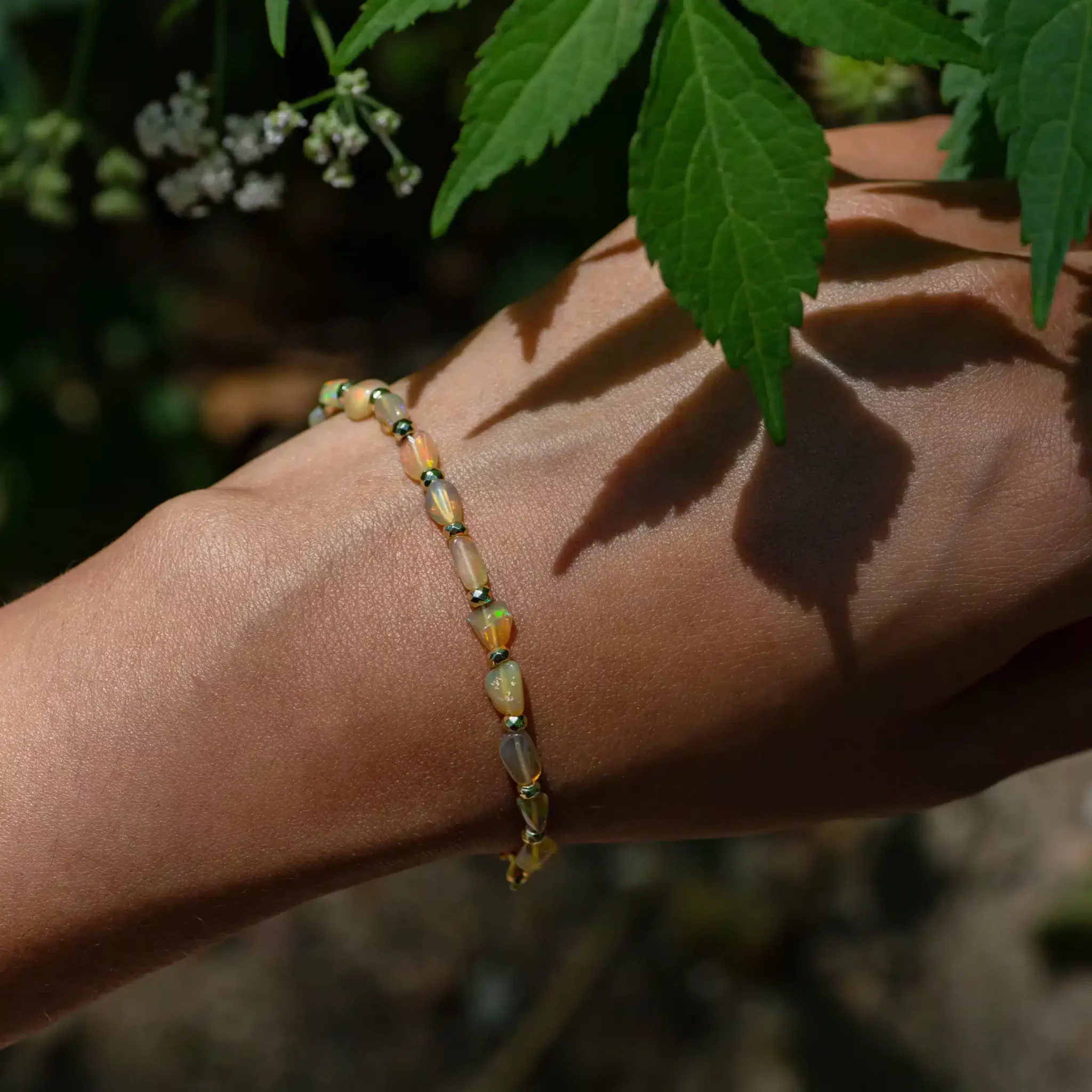bracelet-opale-ethiopie6-scaled-1.webp Bracelet de perles sur poignet près de feuilles vertes