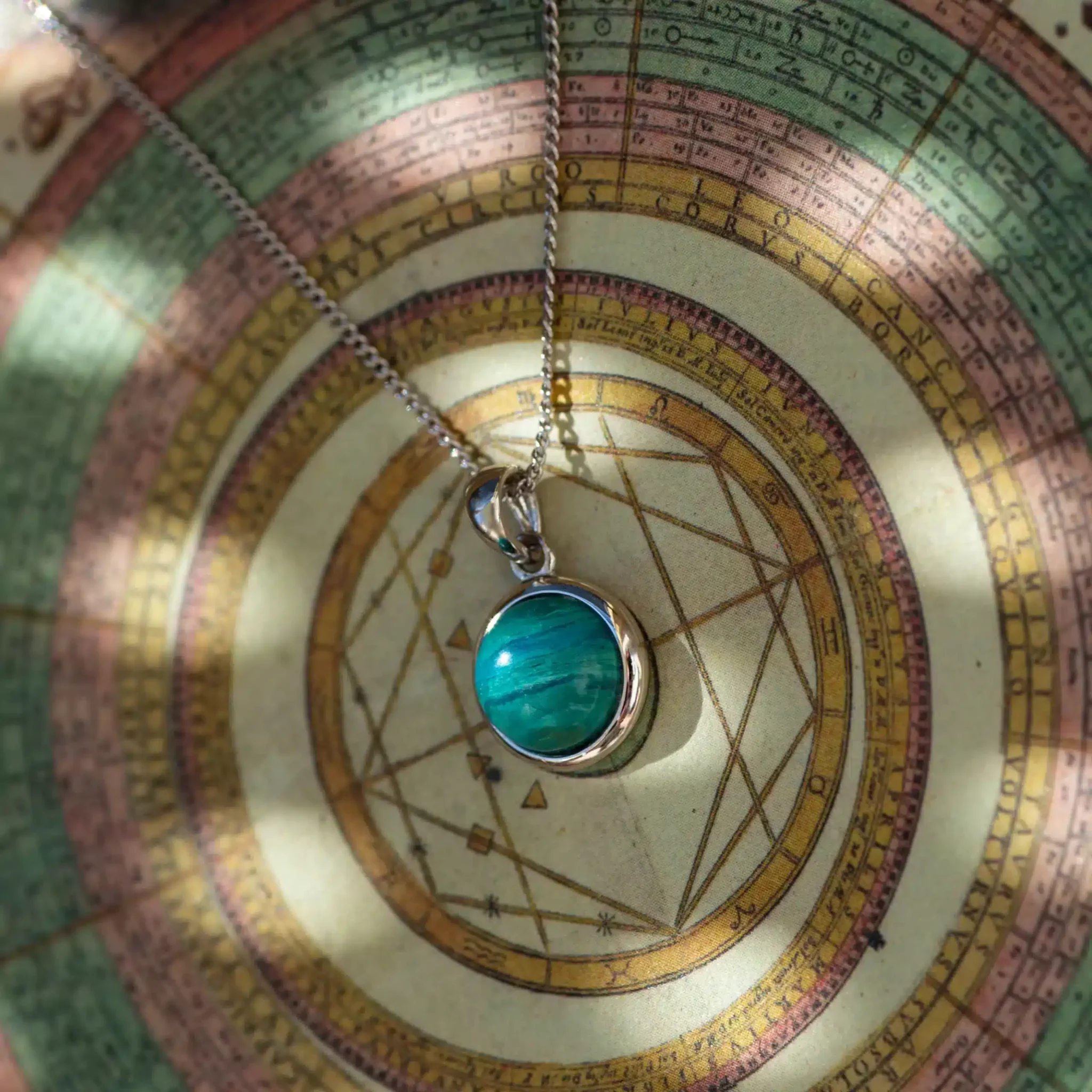 pendentif-opale-verte2-scaled-1.webp Pendentif turquoise posé sur une carte céleste ancienne
