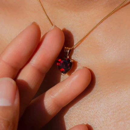 Pendentif cœur rouge sur chaîne dorée, tenu entre doigts