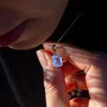 Personne tenant un pendentif rectangulaire bleu sur chaîne dorée